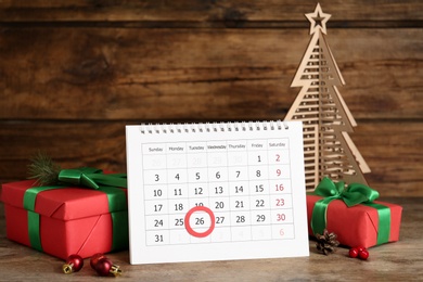Calendar with marked Boxing Day date near gifts and decorative Christmas tree on wooden table