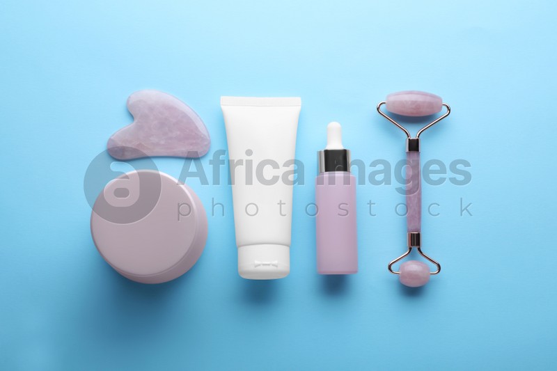 Natural face roller, gua sha tool and cosmetic products on light blue background, flat lay