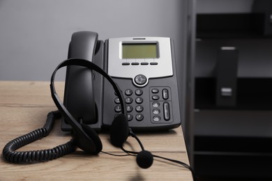 Photo of Stationary phone and headset on wooden desk indoors. Hotline service