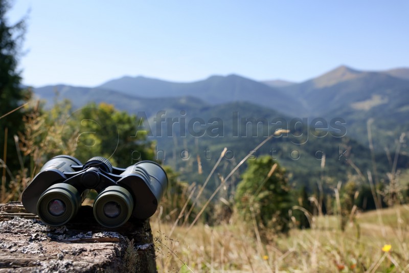 Modern binoculars on wooden surface in mountains, space for text