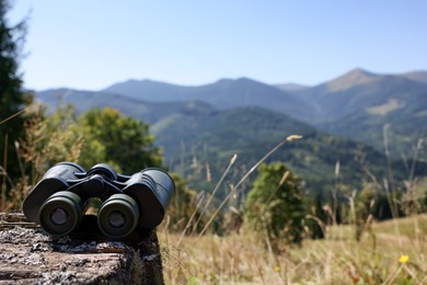 Modern binoculars on wooden surface in mountains, space for text