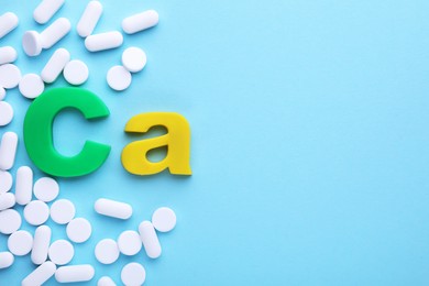 Calcium symbol made of colorful letters and white pills on light blue background, flat lay. Space for text