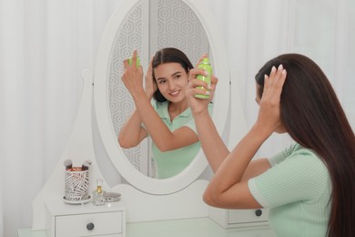 Woman applying dry shampoo onto her hair near mirror at home