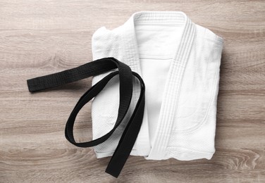 Martial arts uniform and black belt on wooden background, top view