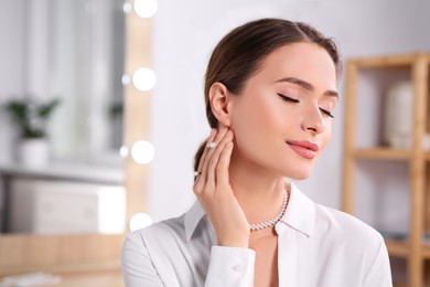 Young woman wearing elegant pearl jewelry indoors, space for text