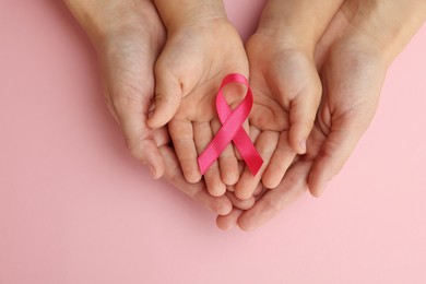 Woman and child holding pink ribbon on color background, top view. Breast cancer awareness