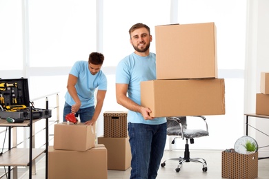 Young worker with cardboard boxes and his colleague in office. Moving service