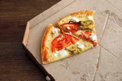 Cardboard box with tasty pizza slices on wooden background