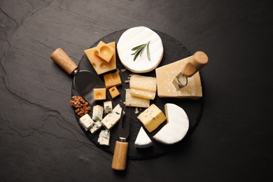 Cheese platter with specialized knives and fork on black table, flat lay