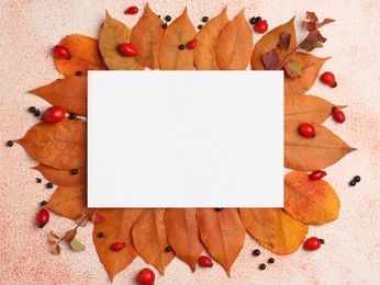 Photo of Yellowed leaves, berries and blank paper card on beige textured background, flat lay