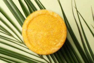Orange solid shampoo bar and leaf on green background, top view. Hair care