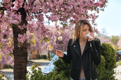 Photo of Woman suffering from seasonal pollen allergy near blossoming tree outdoors
