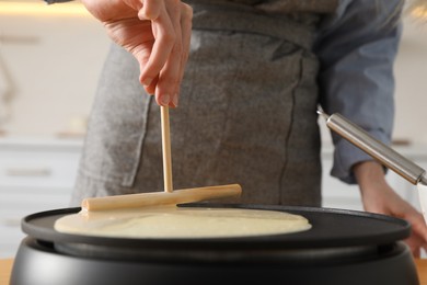 Photo of Woman cooking delicious crepe on electrical pancake maker in kitchen, closeup