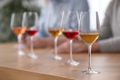 Different sorts of wine in glasses prepared for tasting and sommeliers at wooden table indoors, closeup
