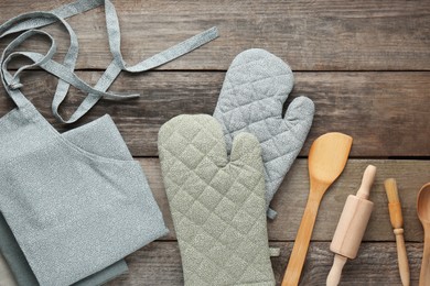 Kitchen napkin, apron, gloves and different utensils on wooden table, flat lay