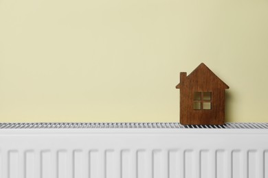 Wooden house model on heating radiator near beige wall, space for text. Energy efficiency concept