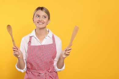 Photo of Beautiful young woman in clean striped apron with kitchen tools on orange background. Space for text