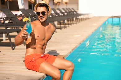 Young man with cocktail near pool on sunny day