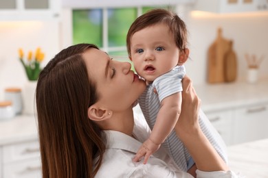 Photo of Happy mother kissing her little baby in kitchen