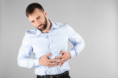 Young man suffering from abdominal pain on light background