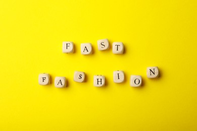 Wooden cubes with phrase Fast Fashion on yellow background, flat lay