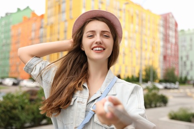 Photo of Beautiful young woman in stylish hat taking selfie outdoors