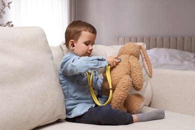 Cute little boy playing with stethoscope and toy bunny at home. Future pediatrician