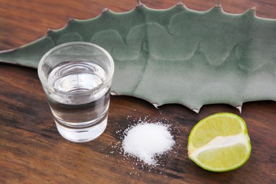 Photo of Mexican tequila shot, salt, lime and green leaf on wooden table, closeup. Drink made of agava