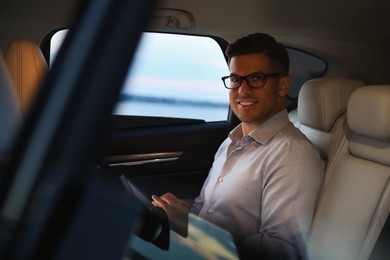 Handsome man using tablet on backseat of modern car