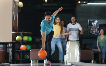 Young man throwing ball and spending time with friends in bowling club
