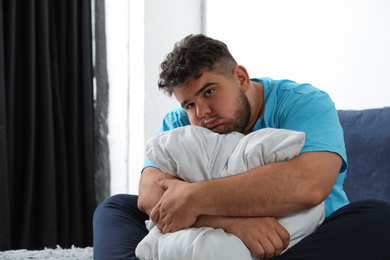 Depressed overweight man hugging pillow on bed