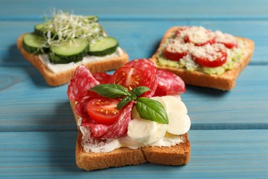 Photo of Tasty toasts with different toppings on light blue wooden table, closeup