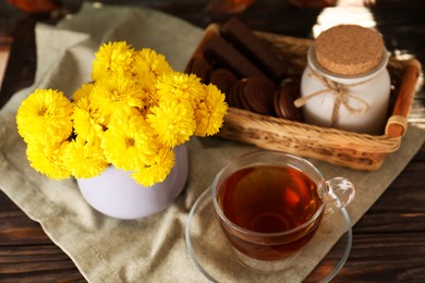 Photo of Beautiful yellow chrysanthemum flowers, cup of aromatic tea and sweet chocolate treats on wooden table