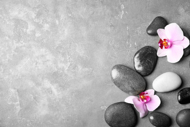 Photo of Stones with orchid flowers and space for text on grey background, flat lay. Zen lifestyle