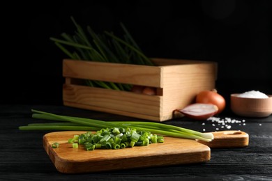 Chopped green spring onion and stems on black wooden table