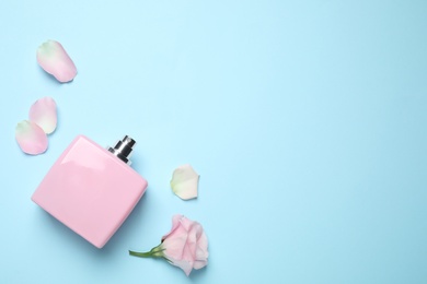 Flat lay composition with bottle of perfume and flower on light blue background, space for text