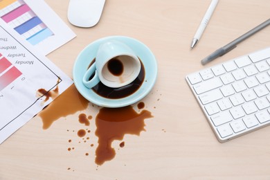 Cup with saucer and coffee spill on wooden office desk, above view