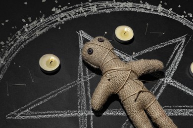 Voodoo doll pierced with pins and candles in pentagram on table