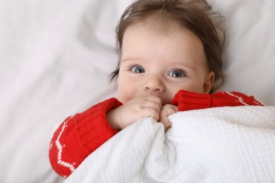 Photo of Cute little baby in Christmas sweater on soft bed, top view