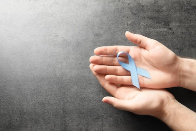 Photo of Man holding blue ribbon on grey background, top view. Cancer awareness