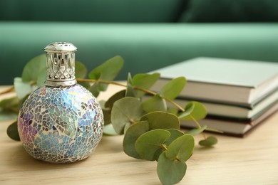 Stylish catalytic lamp with eucalyptus and books on wooden table in living room, closeup. Cozy interior