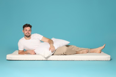 Man with pillow lying on soft mattress against light blue background