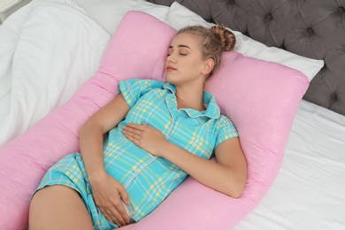 Beautiful pregnant woman sleeping with maternity pillow on bed at home