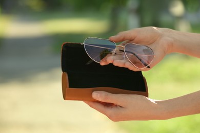 Woman holding sunglasses and case on blurred background, closeup