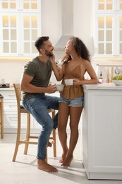 Lovely couple with cups of drink enjoying time together in kitchen at home