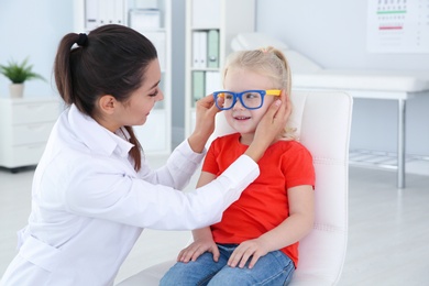 Children's doctor putting glasses on little girl in clinic