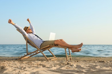 Photo of Happy man with laptop resting on deckchair near sea. Business trip