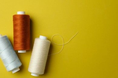 Different colorful sewing threads on yellow background, flat lay. Space for text
