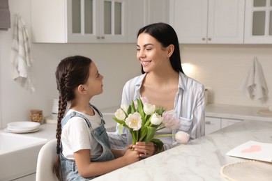 Photo of Little daughter congratulating her mom at table in kitchen. Happy Mother's Day