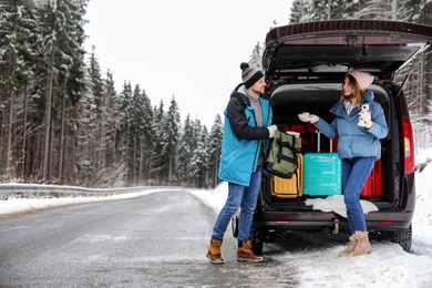 Couple near open car trunk full of luggage on road, space for text. Winter vacation